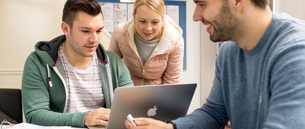 Drei Studierende arbeiten gemeinsam an einem Laptop.