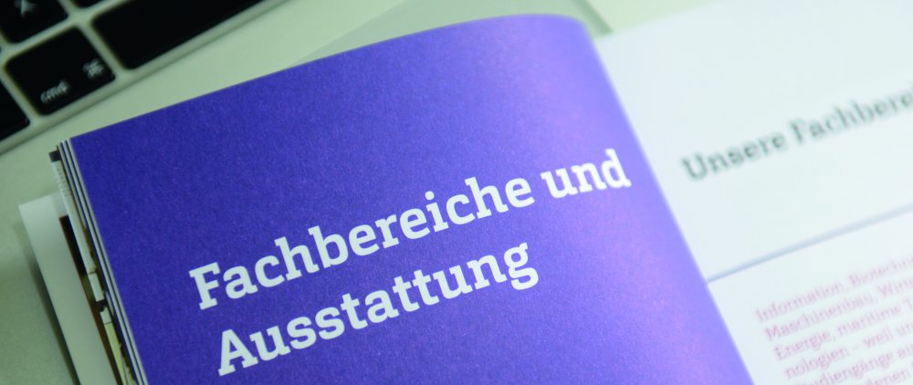 Hochschulbroschüre auf der Seite "Fachbereiche und Ausstattung" aufgeschlagen. Am oberen Bildrand ist eine Tastatur zu erkennen.