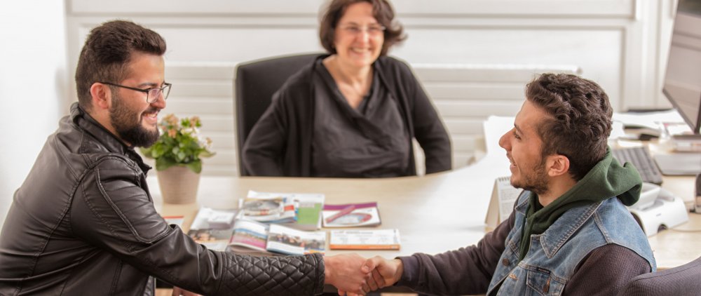 Beratungsgespräch mit zwei Geflüchteten, die sich im Bildvordergrund die Hand reichen.