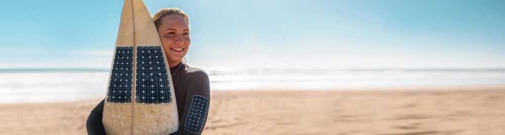 Junge Surferin an einem Strand hält ein Surfbrett mit Solarzellen