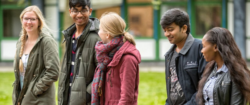 Gruppe von 5 Studierenden, die ins Gespräch vertieft über den Campus gehen.