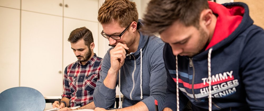 Drei Studenten während eines Seminars, über Schreibblöcke gebeugt und schreibend.