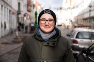 Ein junger Mann mit schwarzer Mütze und Brille steht in der Flensburger Norderstraße.
