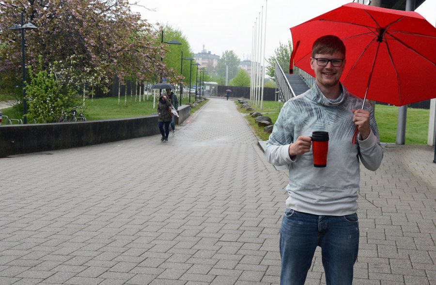 Student Bror mir Regenschirm und Keffeebecher in leuchtendem Rot auf dem Platz vor dem audimax.