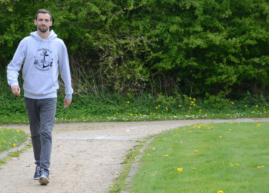 Student Marcel läuft über den Campus. Im Hintergrund viel Grün.