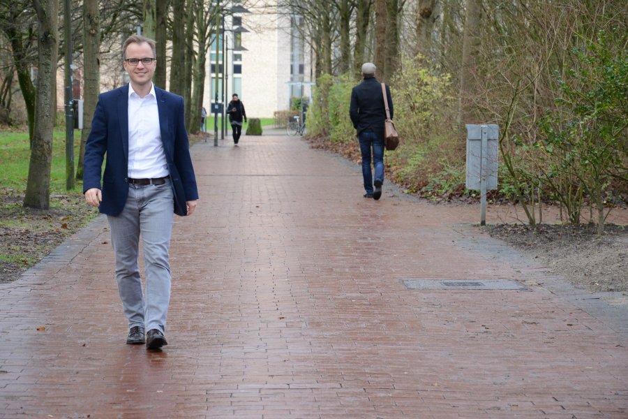 Jan Gerken auf dem Campus. Im Hintergrund Bäume und ein Gebäude.