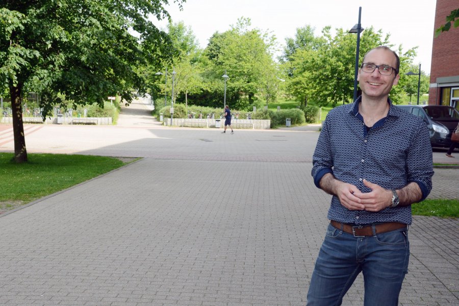 Sven Bertel auf dem Campus. Im Hintergrund Bäume und ein Hochschulgebäude.