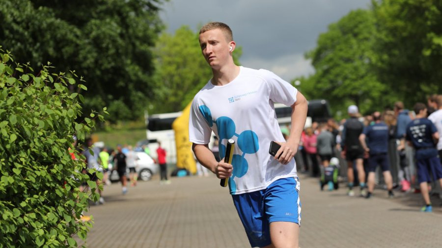 Ein junger Mann joggt am Fotografen vorbei, er trägt einen Staffelstab und ein Trikot der Schleswig-Holstein Netz GmbH.