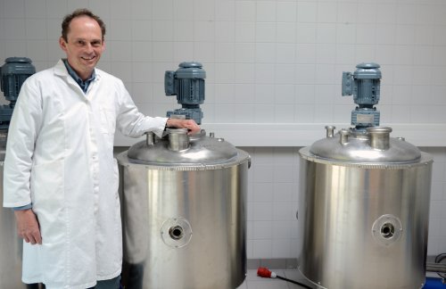 Hinrich Uellendahl steht im Laborkittel vor zwei großen silbernen Behältern.