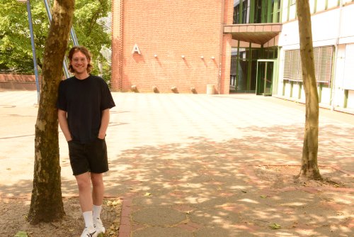 Ben lehnt an einem Baum auf dem Campus der Hochschule Flensburg.