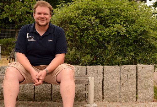 Jonas sitzt auf einer Bank auf dem Campus der Hochschule Flensburg.