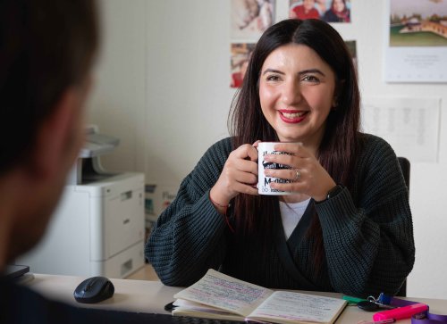 Eine Frau sitzt mit Tasse in der Hand am Schreibtisch, im Gespärch 