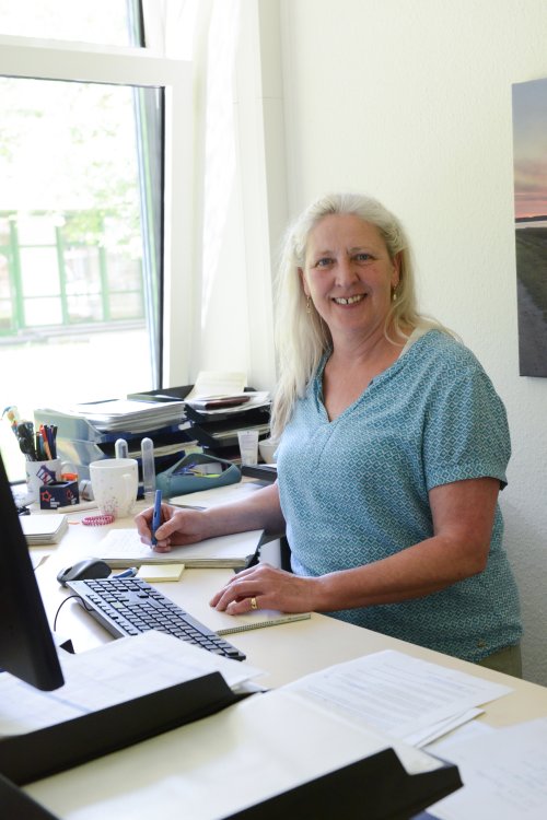 Iris Mainusch sitzt am Schreibtisch und schaut in die kamera