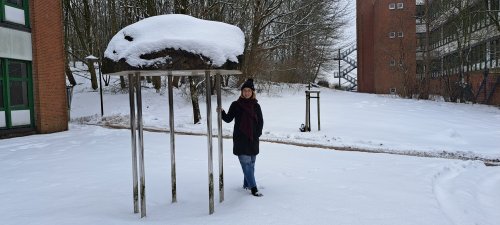 Eine Studentin steht auf dem Flensburger Campus im Schnee neben einer Skulptur.
