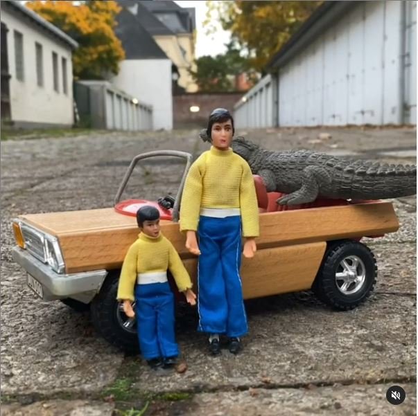 Zwei Spielfiguren lehnen an einem gelben Auto.