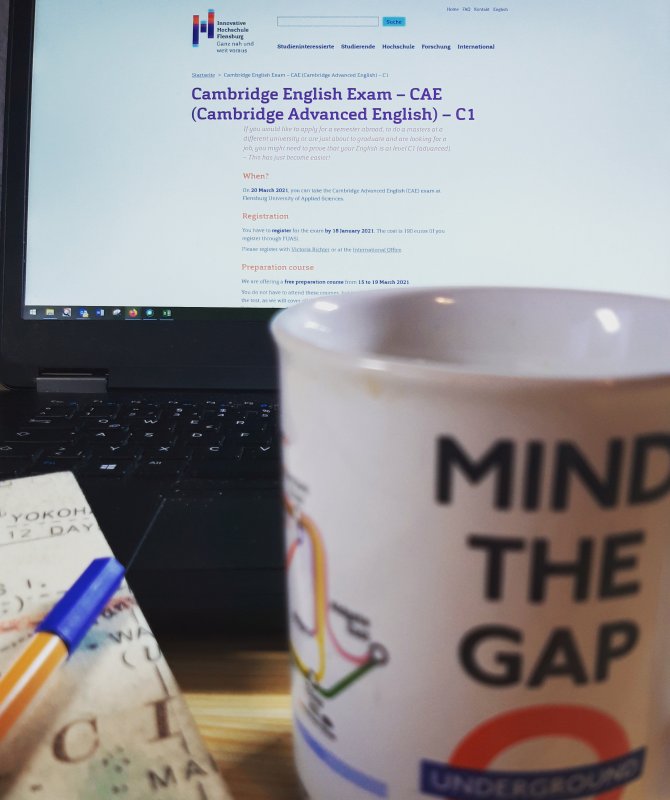 Vorn im Bild unscharf eine Tasse mit Londoner U-Bahn-Motiv, dahiner ein Laptop auf dessen Bildschirm eine Seite zum CAE-Test zu erkennen ist.