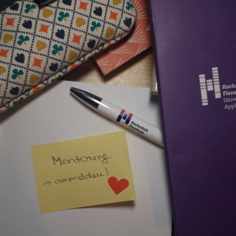 Weißes Blatt mit Post It, auf dem "Mentoring" steht, daneben ein Herz. Drum herum Stift, Federmappe, Notizbücher.