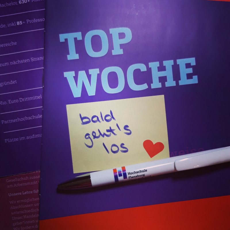 Ein lila Flyer, auf dem TOP Woche steht, darauf ein Stift und Post It mit der Aufschrift "bald geht's los".