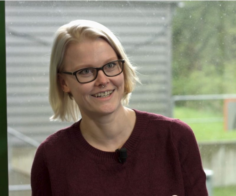Junge Frau schaut und spricht in die Kamera. Sie lacht.