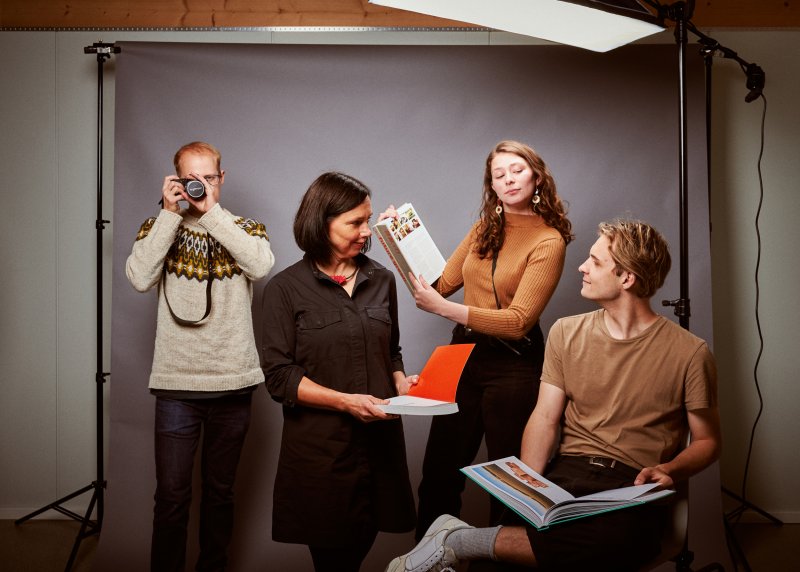 Vier menschen posieren in einem Fotostudio, sie halten eine Kamera, Druckproben und ähnliches.
