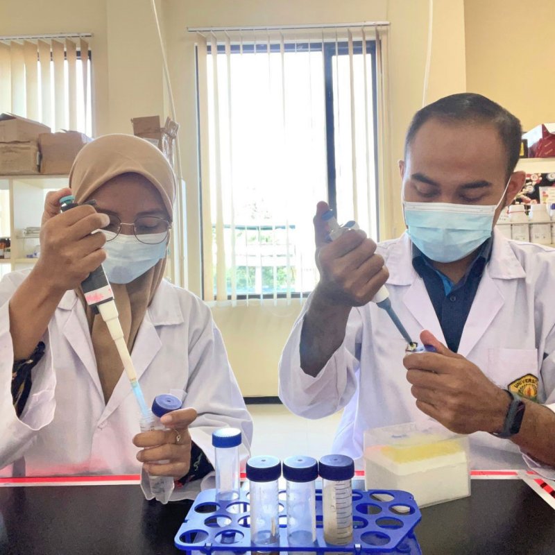 Zwei Studierende mit Kittel und Maske im Labor. Sie pipettieren.