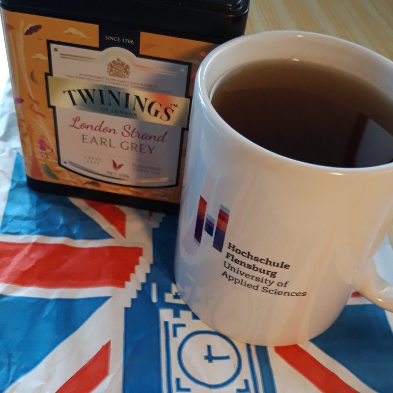 Eine Tasse mit Hochschullogo und eine Teedose stehen auf einem Untersetzer in britischen Farben und Motiv.