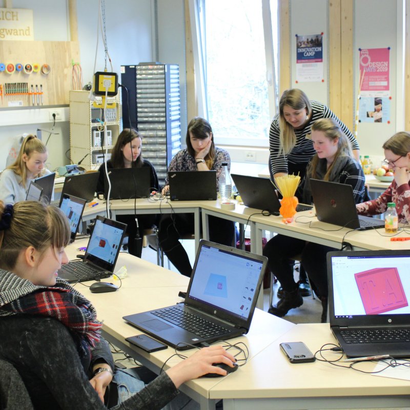 Mädchen sitzen um einen Tisch und arbeiten an Computern.