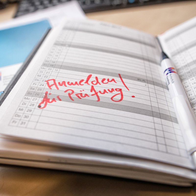 Aufgeschlagener Kalender, in roter Schrift: Anmeldung zur Prüfung!