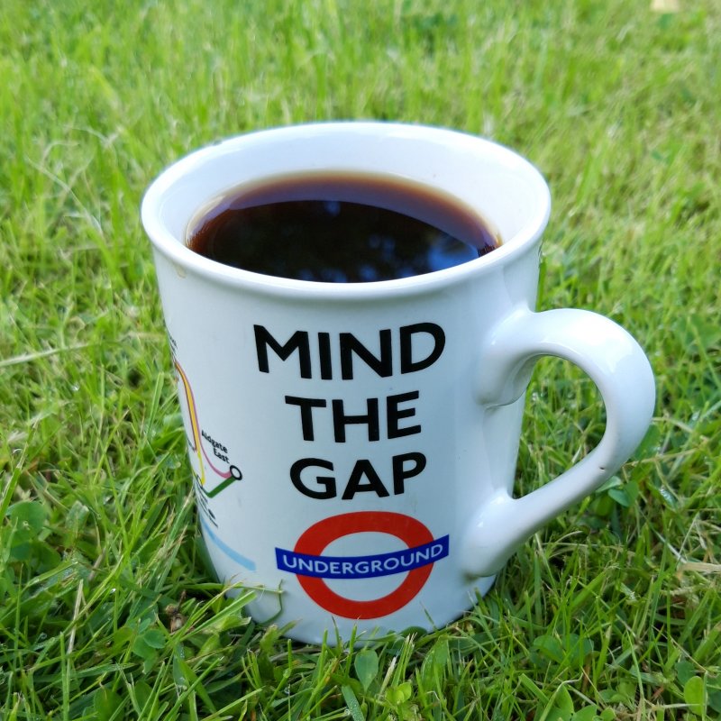 Mit Kaffee gefüllte Tasse mit Motiv der Londoner U-Bahn auf einer grünen Wiese.