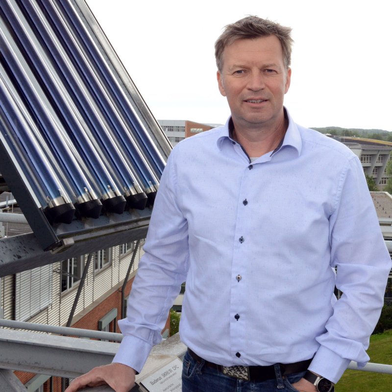 Ilja Tuschy steht auf einem Dach, hinter ihm Solarzellen.