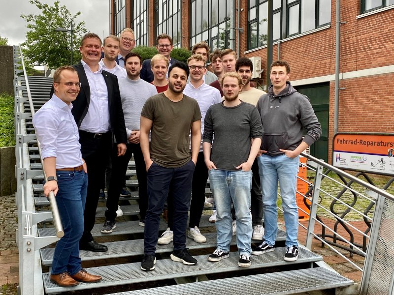 Gruppe von Studierenden und Lehrenden posieren auf einer TReppe. Sie lachen in die Kamera.