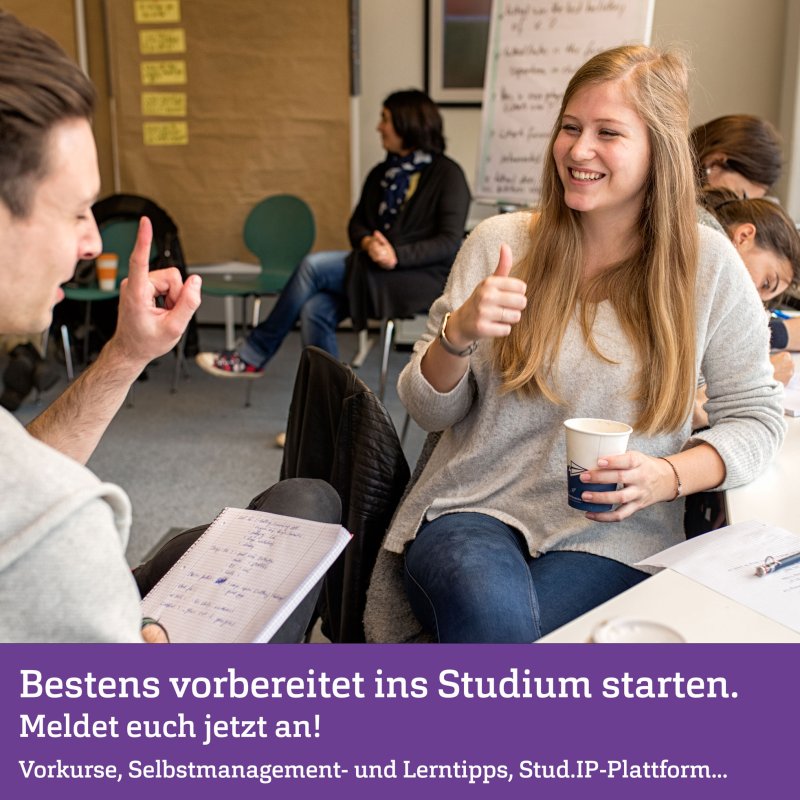 Im Vordergrund zwei junge Menschen, eine hebt den Daumen nach oben. Neben ihnen ein Tisch mit Zetteln, im Hintergrund sind andere Menschen in einer Lernsituation zu erkennen.