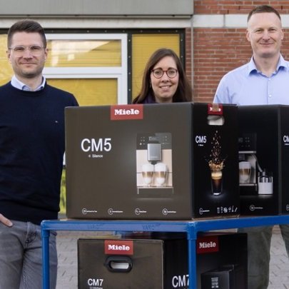 Zwei Männer und eine Frau stehen um einen Tisch mit einem Karton eines Miele Kaffee-Vollautomaten.