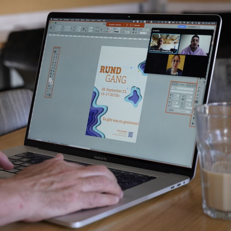 Nahaufnahme eines Laptop-Bildschirms, an dem ein Poster mit dem Schriftzug "Rundgang" grafisch gestaltet wird. In der Ecke sieht man in Videocall-Kacheln drei Studierende.