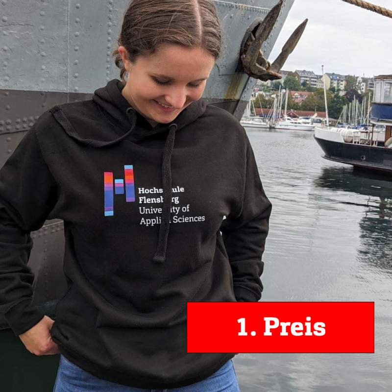 Eine junge Frau in einem schwarzen Hoodie mit dem Logo der Hochschule Flensburg, im Hintergrund der Flensburger Hafen.