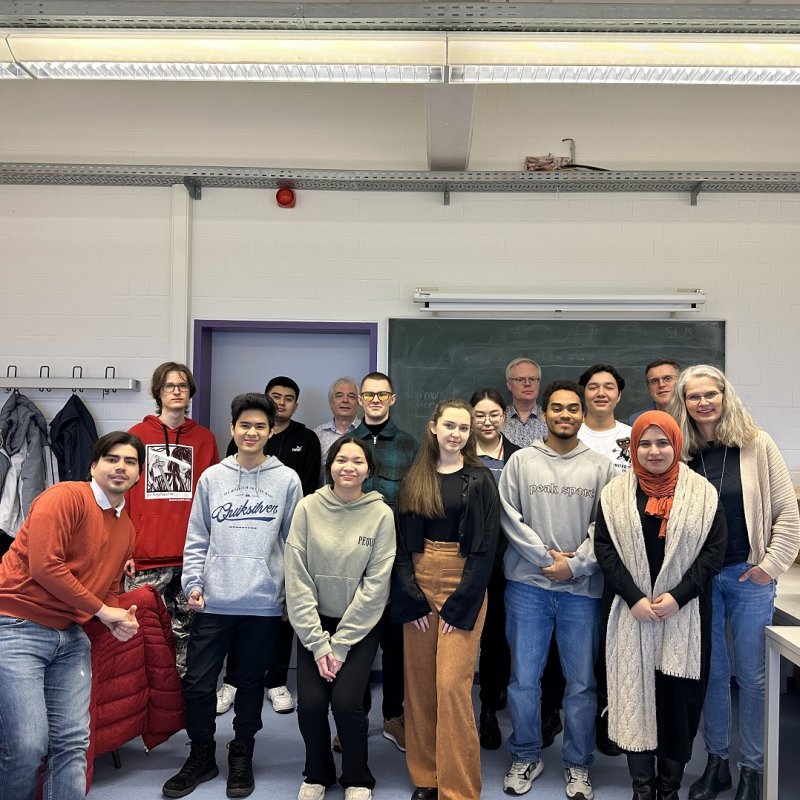 Eine Gruppe von jungen Menschen verschiedener Ethnien steht in einem Klassenraum vor einer Schultafel und lächelt in die Kamera.