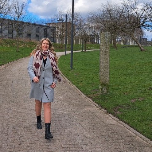 Eine junge Frau läuft über den Flensburger Campus, im Hintergrund grüne Wiesen und Bäume.