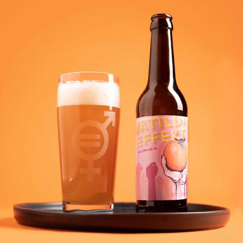 Auf einem Tablett eine braune Bierflasche mit rosenem Etikett, darauf in gelber Schrift "Matilda Effekt" und eine Grafik von vielen Fäusten, die in die Luft gestreckt sind, eine davon hält eine Orange. Daneben ein Bierglas mit einem kombinierten Männlich- und Weiblich-Symbol, in dem ein Gleichheitszeichen steht.