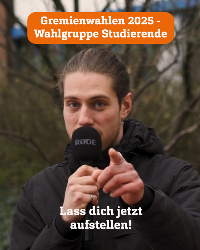 Ein junger Mann in schwarzer Jacke und mit langen, zu einem dutt gebundenen Haaren spricht in ein Mikrofon und zeigt dabei mit dem Finger in die Kamera.