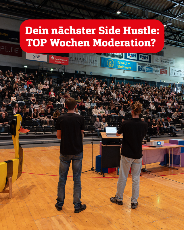 Zwei junge Männer stehen mit dem Rücken zum Fotografen, mit Blick auf eine Sporthallen-Tribüne.
