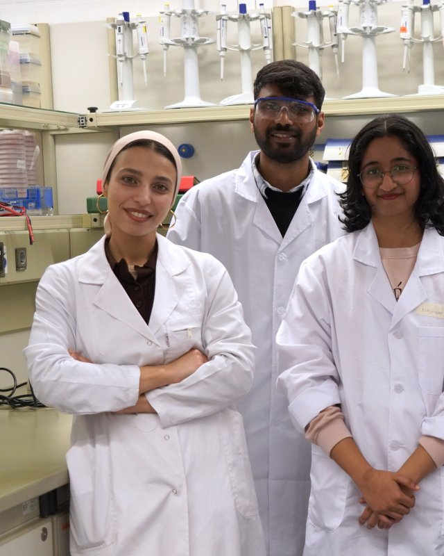 Ausschnitt eines Gruppenbildes: Junge Menschen in Laborkitteln in einem Labor.