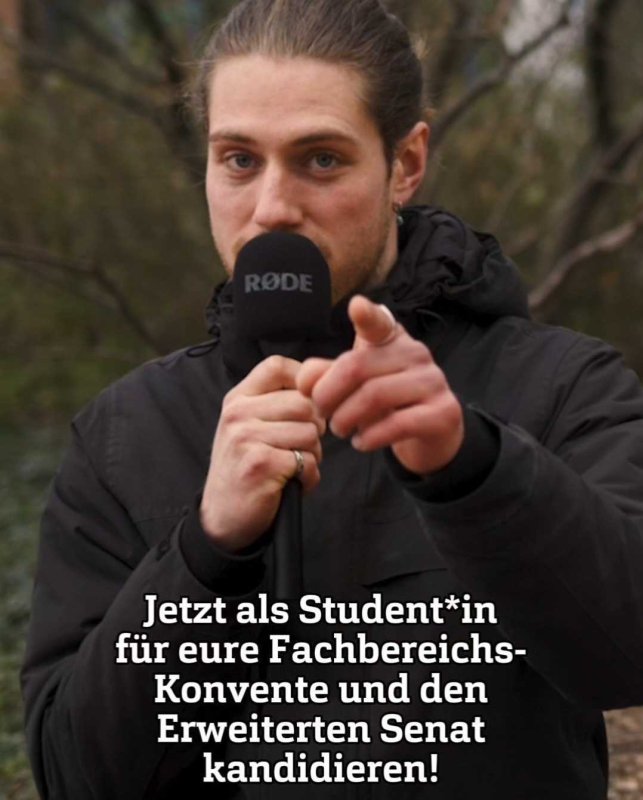 Ein junger Mann spricht in ein Mikrofon und zeigt dabei in die Kamera.