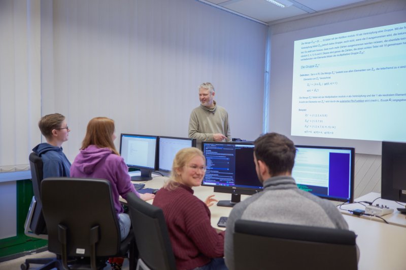 Lehrsituation: Ein Dozent vor einer Gruppe Studierender an Rechnern.
