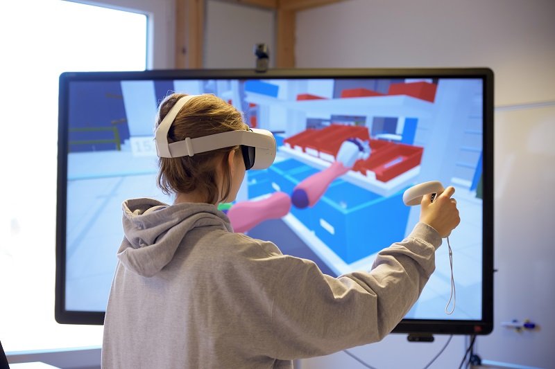 Studentin steht mit VR-Brille vor Monitor.