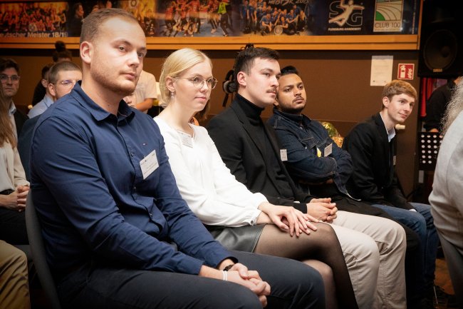 Junge Menschen sitzen nebeneinander und blicken nach vorn.