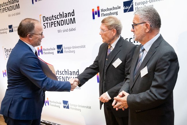 Drei Männer, zwei von ihnen schütteln Hände.