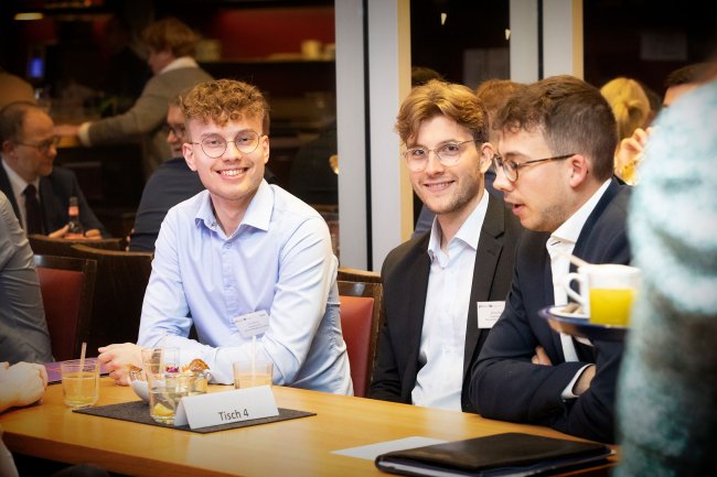 Drei junge Männer an einem Tisch, sie lachen.