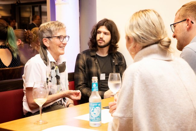 Vier Menschen um einen Tisch, sie unterhalten sich.