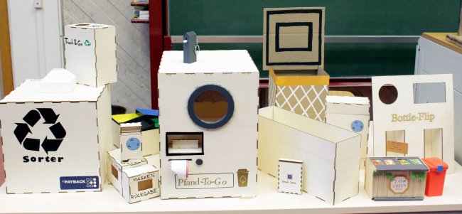 Aufgereihte aus Pappe gebaute Prototypen unterschiedlicher Art.