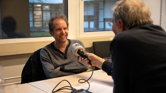 Vigo im Interview. Er sitzt an einem Tisch und spricht in ein Mikrofon.